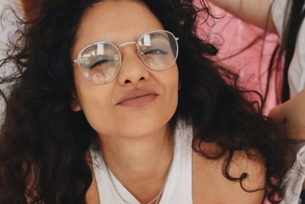 a girl in white tank top smiling while wearing eyeglasses